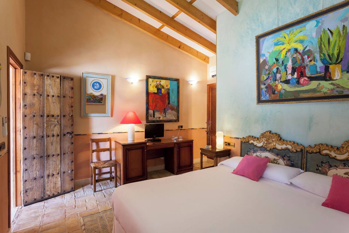 Een hotelkamer met een bed, bureau, stoel en kunstwerken aan de muur.