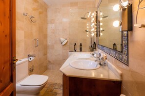 Une salle de bain avec deux lavabos, des toilettes, une douche avec éclairage et un miroir avec éclairage.