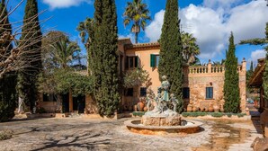 Une cour avec une fontaine, de grands cyprès et un bâtiment doté d’un toit en tuiles.