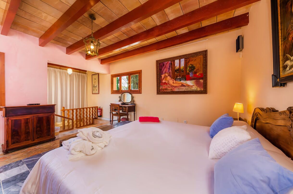 A hotel room with a large bed, a wooden desk, a chair, and a painting on the wall.