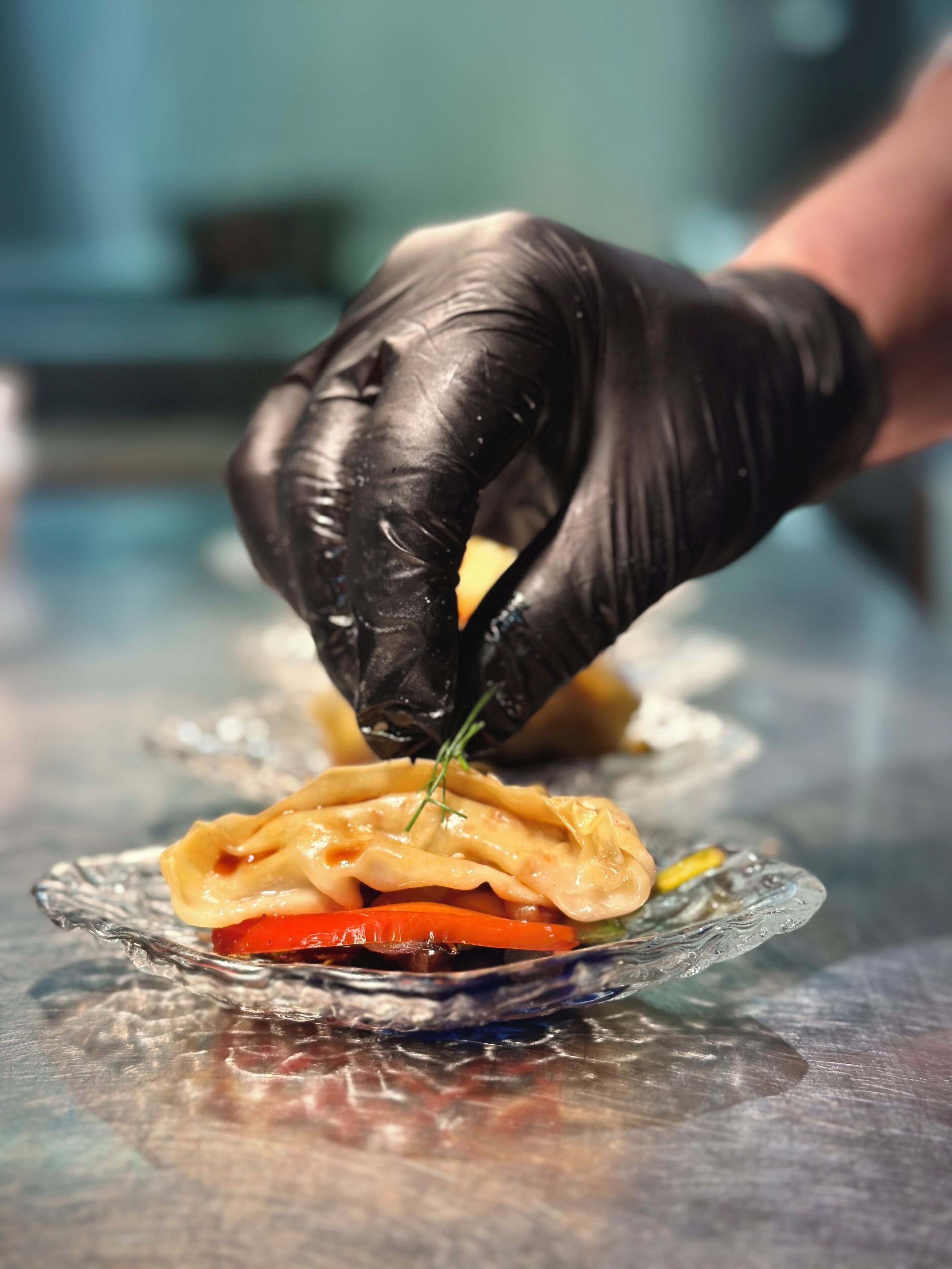 A person wearing black gloves preparing food on a glass plate.