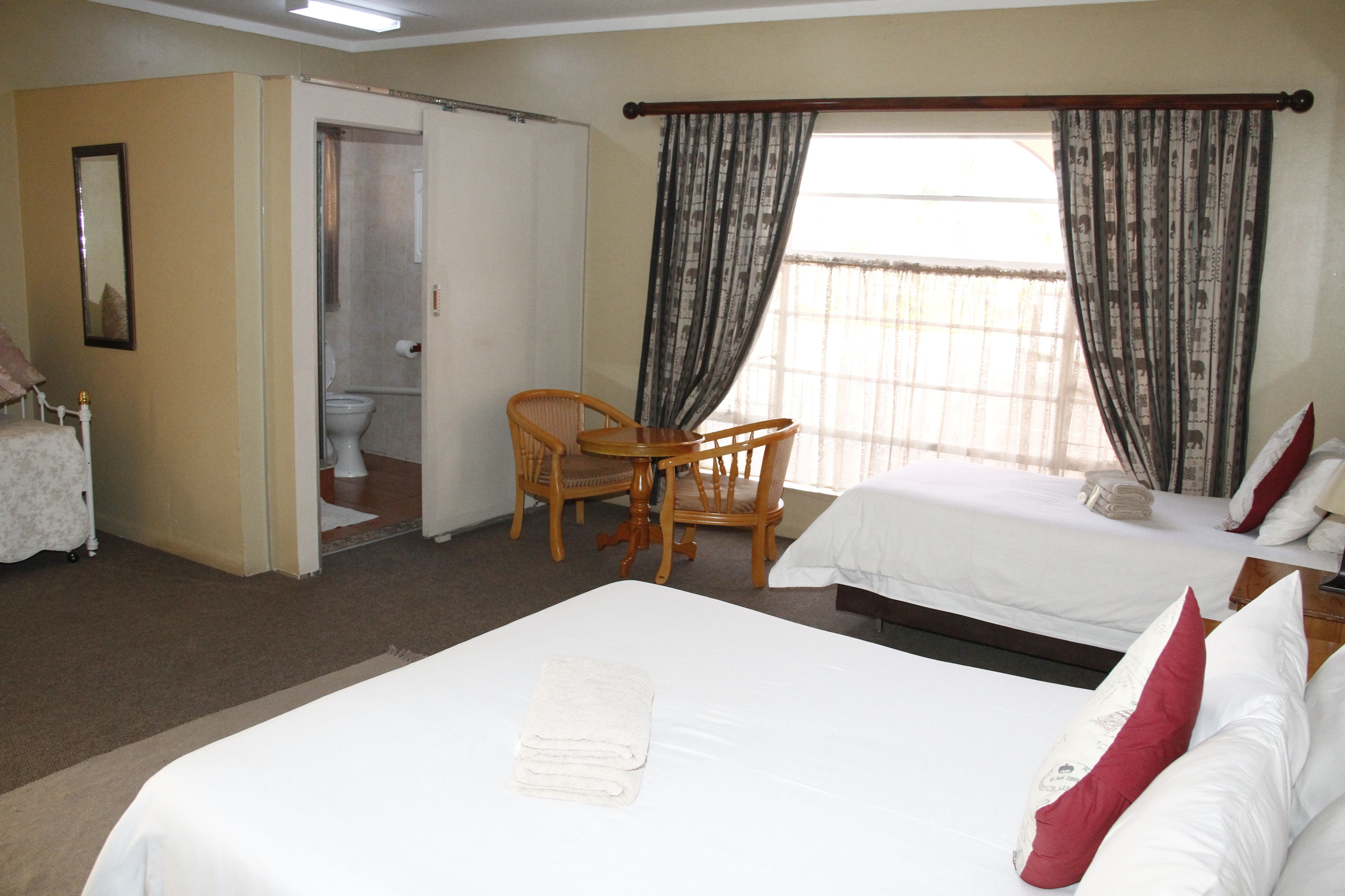 Ein Hotelzimmer mit Bett, Sessel, kleinem Tisch, Bad und Fenster mit Vorhängen.