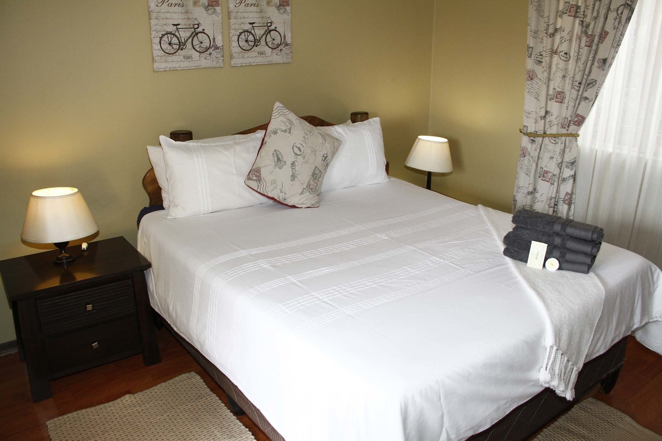 Una cama bien hecha con sábanas blancas, dos lámparas de noche y una almohada con motivos de bicicleta.