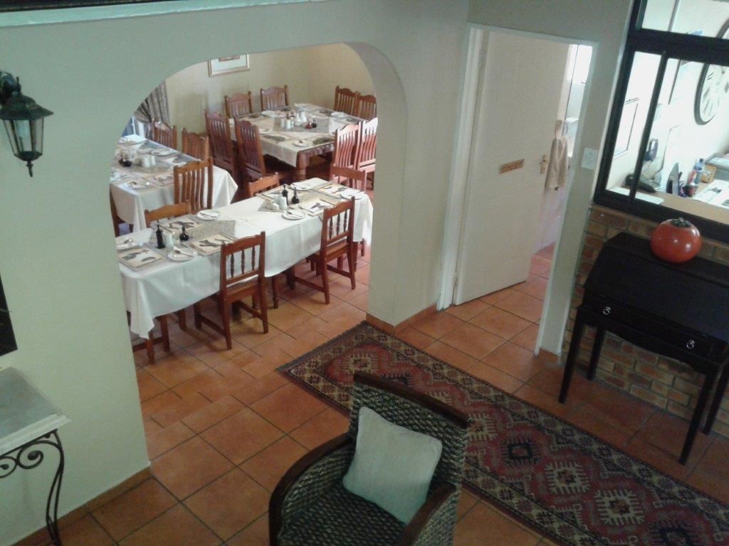 Un comedor con varias mesas y sillas, un tapete estampado y una silla de mimbre con cojín.
