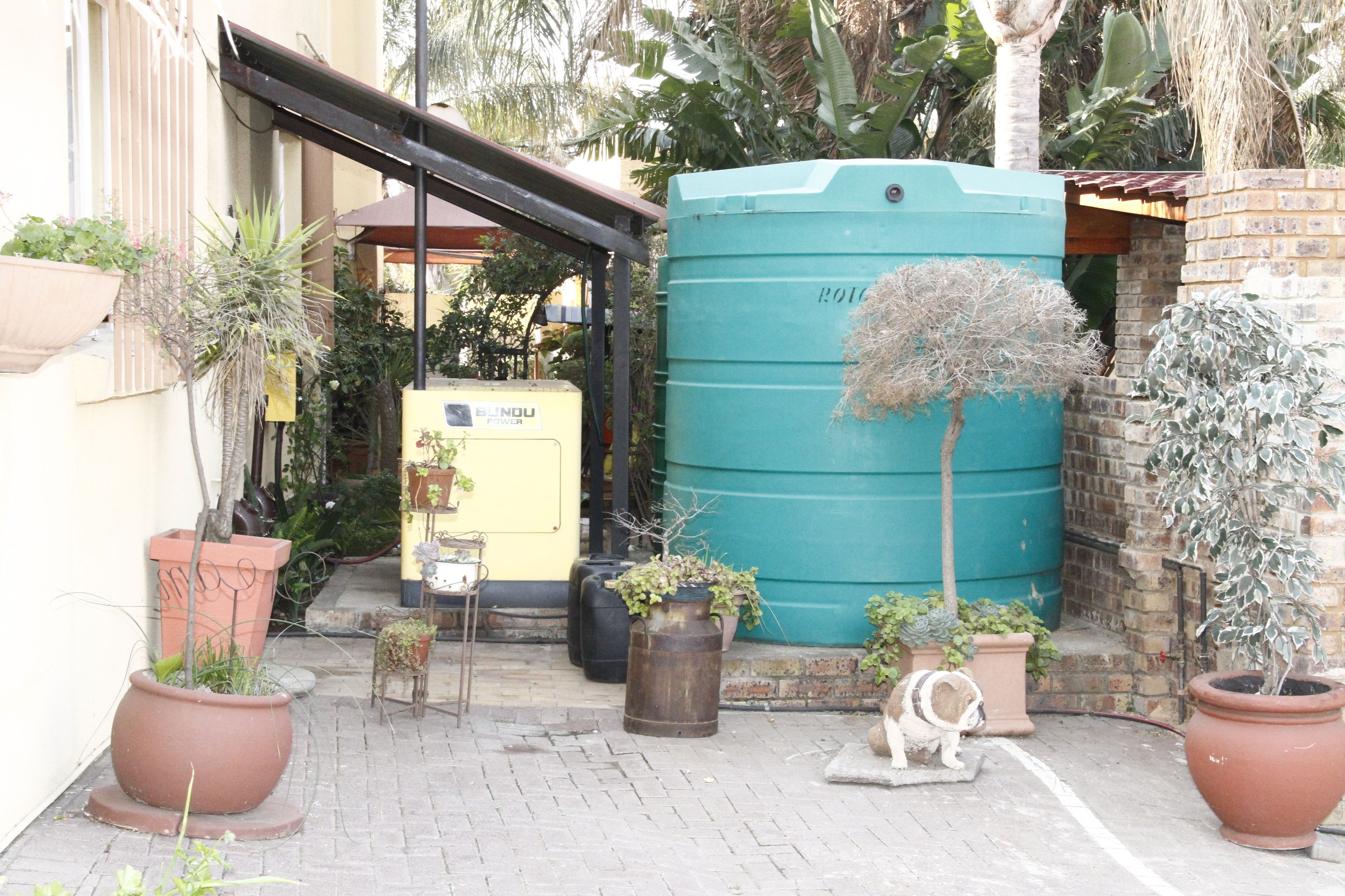 A courtyard with potted plants, a large water tank, and a small statue.