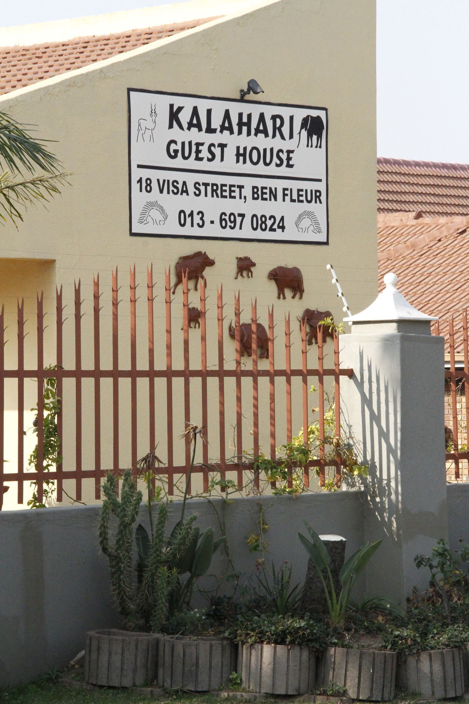 Señal del Kalahari Guest House con datos de contacto y una valla con siluetas de animales.