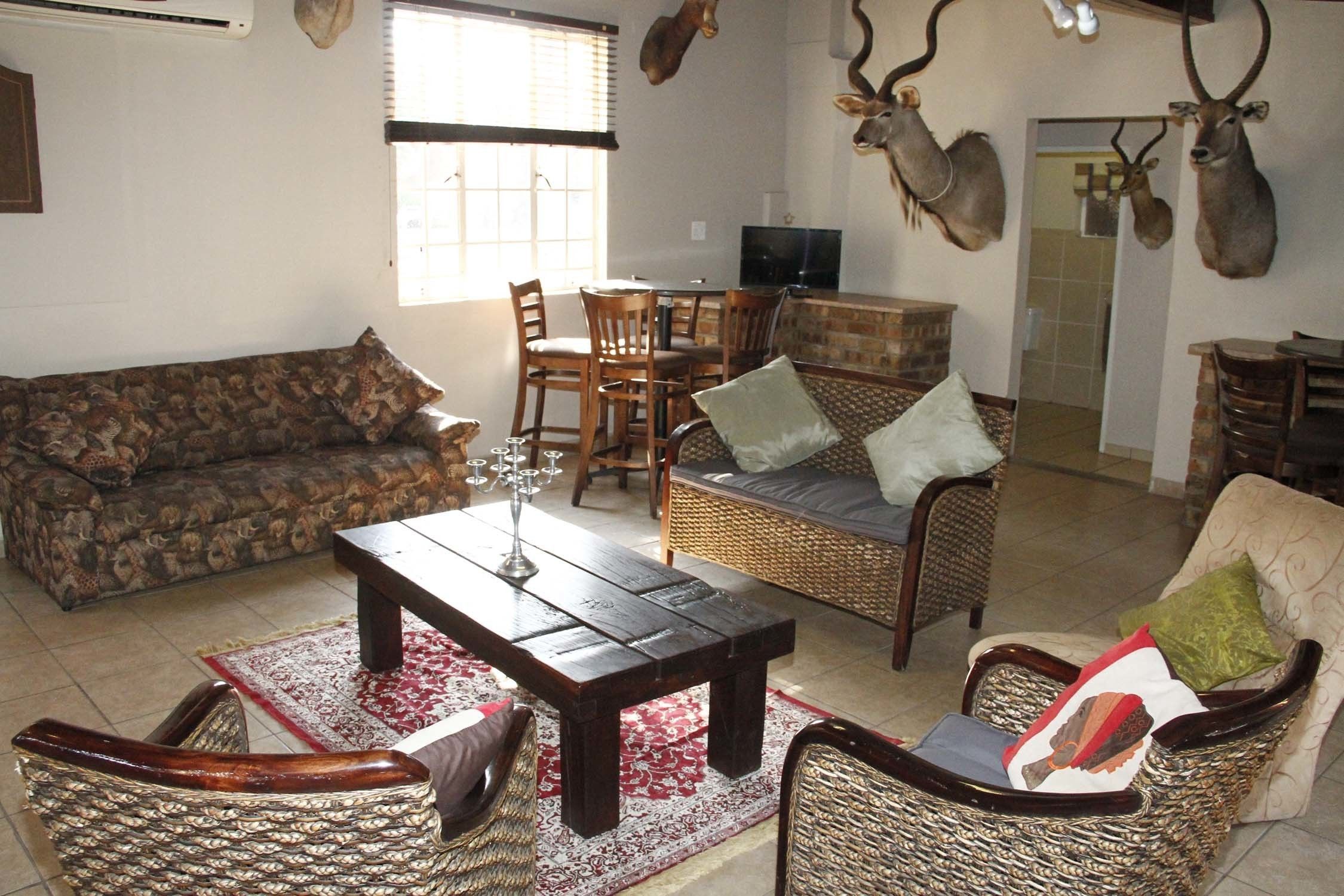 A living room with a sofa, chairs, a coffee table, and a dining area with chairs and a table. There are mounted animal heads on the wall.