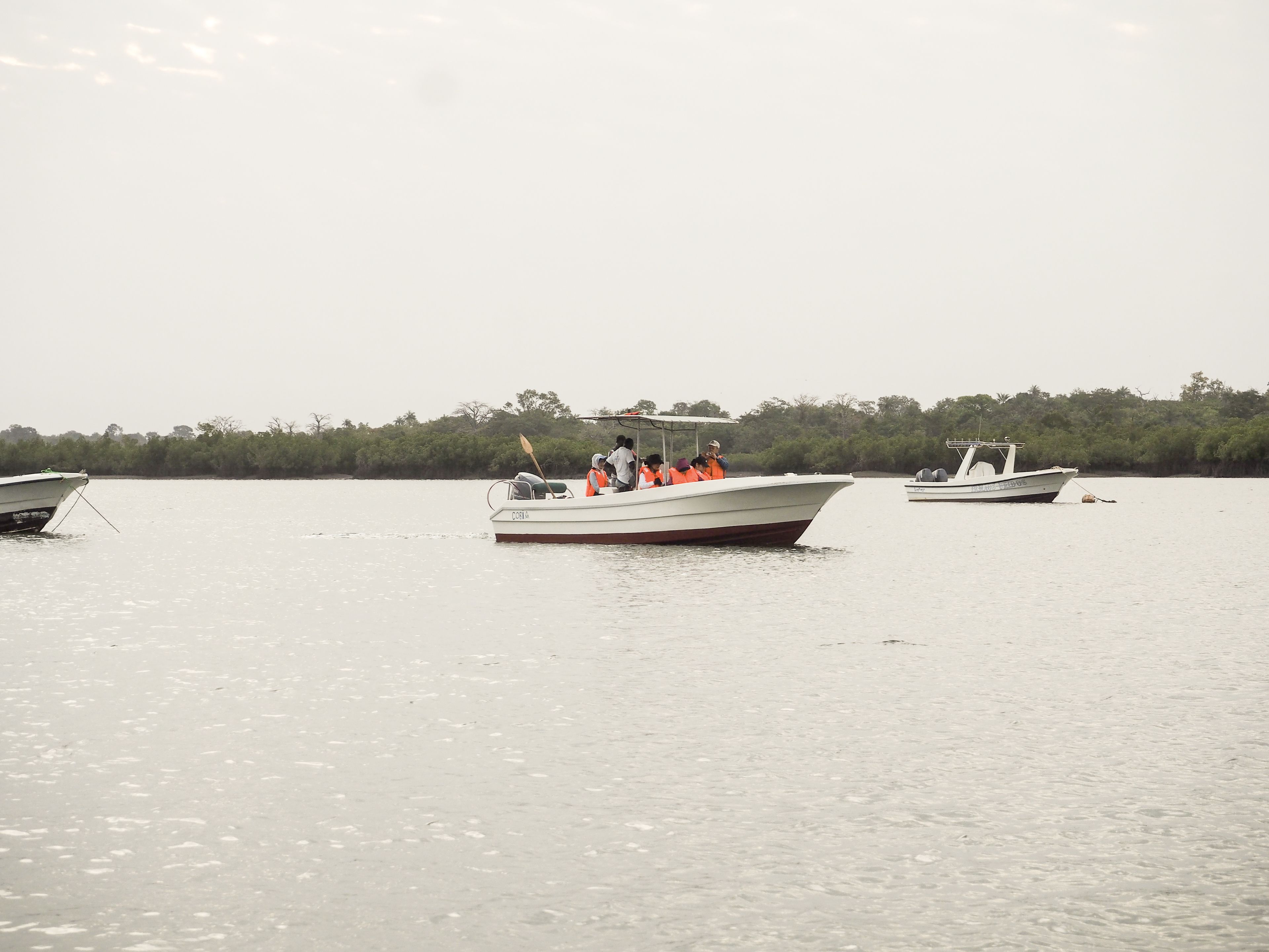 A boat with passengers wearing life jackets on calm water.