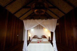 A room with a wooden ceiling, a canopy bed, two bedside lamps, and a nightstand.