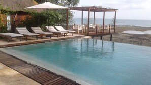 Una piscina infinitària amb gandules i un pont de fusta amb vista al mar.