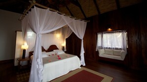 A four-poster bed with a canopy, a bedside table with a lamp, a sofa, and a window with curtains. - Ponta Anchaca (Rubane)