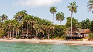 A beachfront property with thatched-roof structures, palm trees, and clear blue water. - Ponta Anchaca (Rubane)
