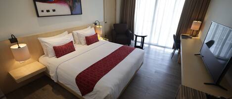 A hotel room with a large bed, a TV, a desk, and a chair.