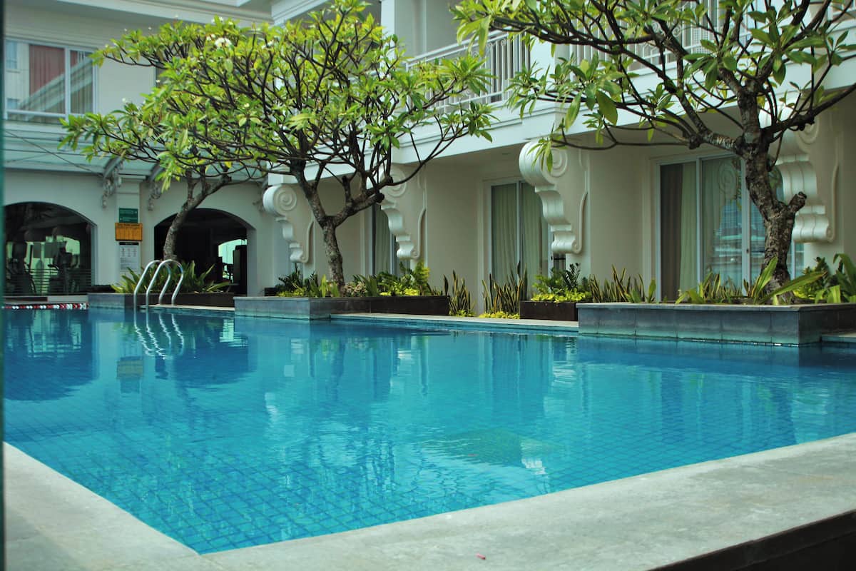 Una piscina con superficie de agua azul cristalina, rodeada por un edificio blanco con balcones y columnas decorativas.