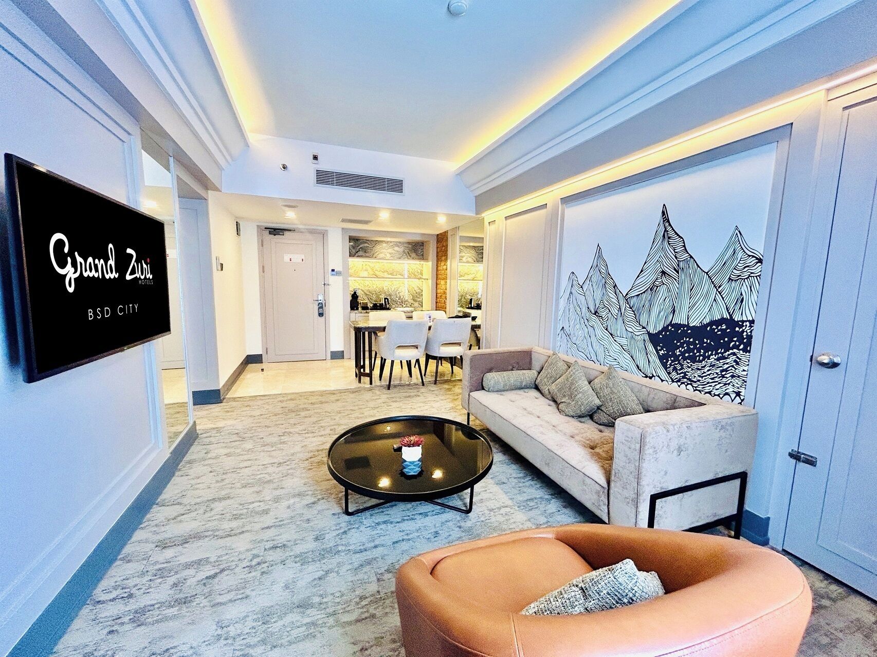 Habitación de hotel con sofá, mesa de centro, televisor, zona de comedor y un mural.