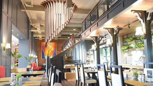A modern restaurant with high ceilings, exposed ductwork, and a mix of seating arrangements including booths and tables.