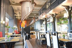 Un restaurant moderne avec de hauts plafonds, des conduits apparents et différents types de sièges, notamment des banquettes et des tables.