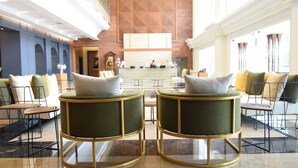 A lobby with a reception desk, two round tables with chairs, and a high ceiling with patterned design.