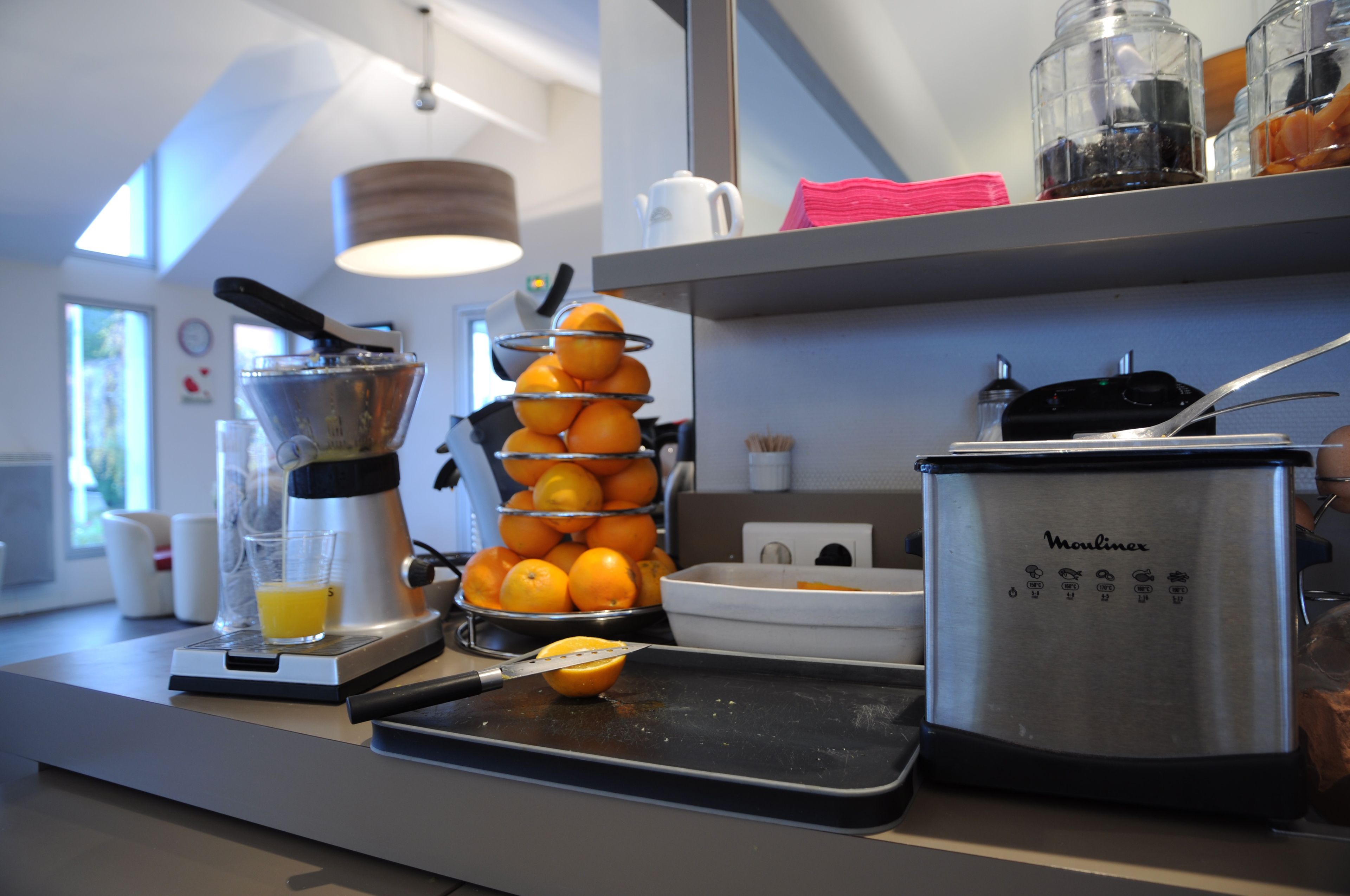 Un taulell de cuina amb un exprés, una prestatgeria de fruita, una batedora i una cafetera.