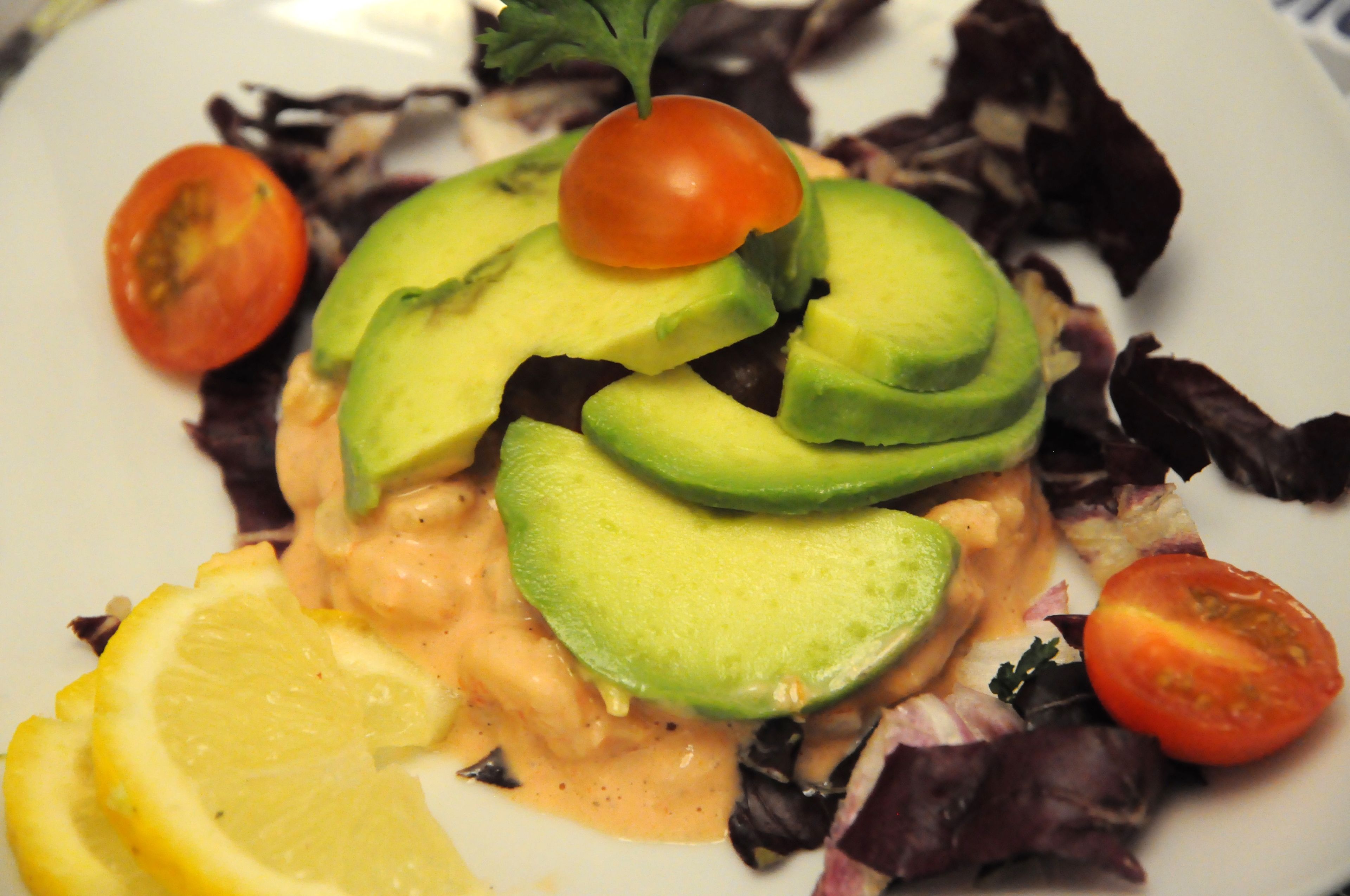 Un plato con rodajas de aguacate, tomates cherry y gajos de limón sobre una cama de hojas verdes variadas.
