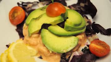 Un plato con rodajas de aguacate, tomates cherry y gajos de limón sobre una cama de hojas verdes variadas.