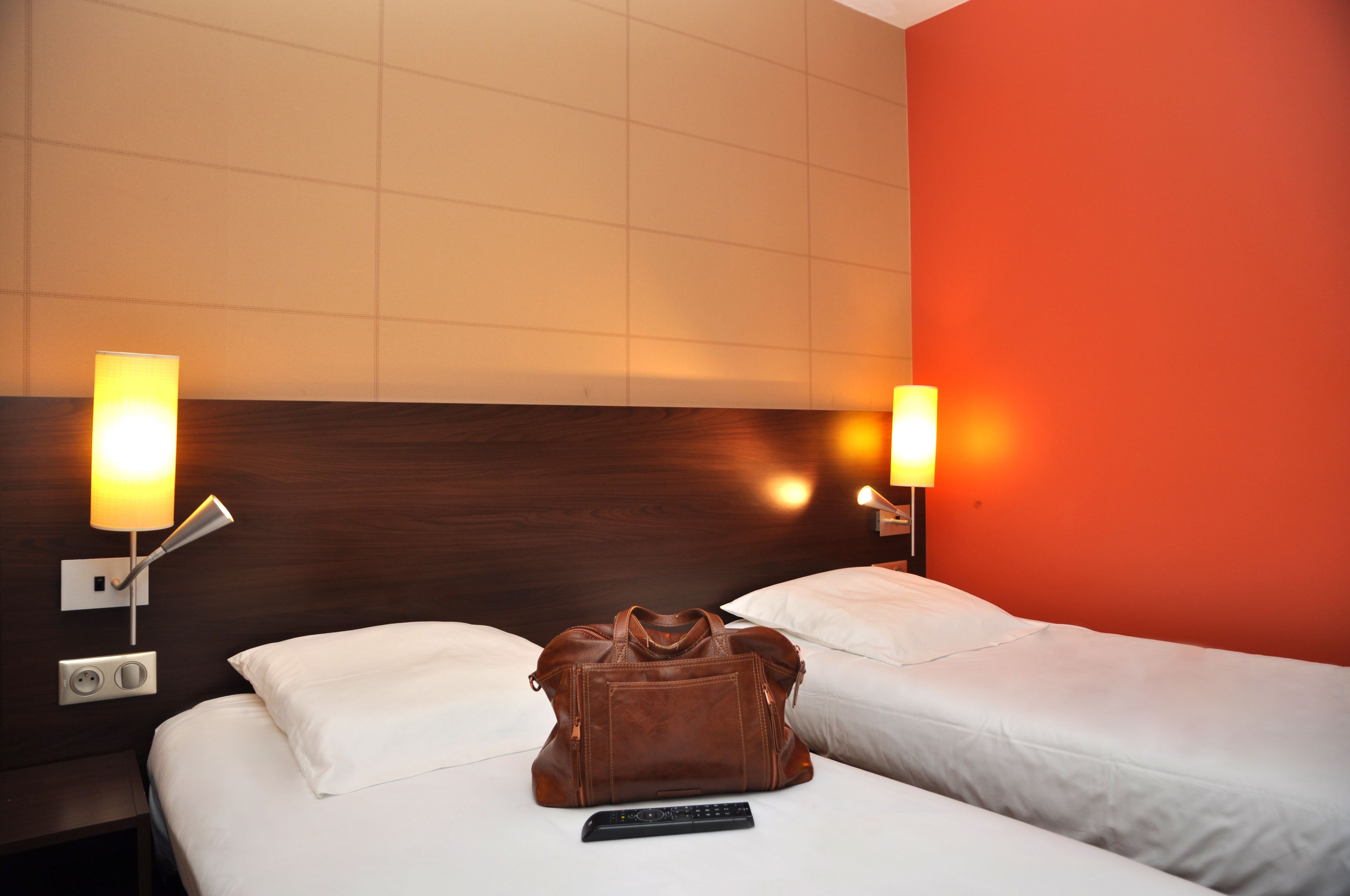 A hotel room with two beds, a brown leather bag, and a remote control on the bed.