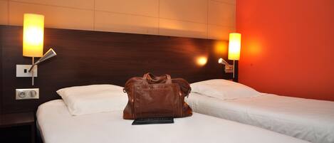 A hotel room with two beds, a brown leather bag on the bed, and wall-mounted lamps.