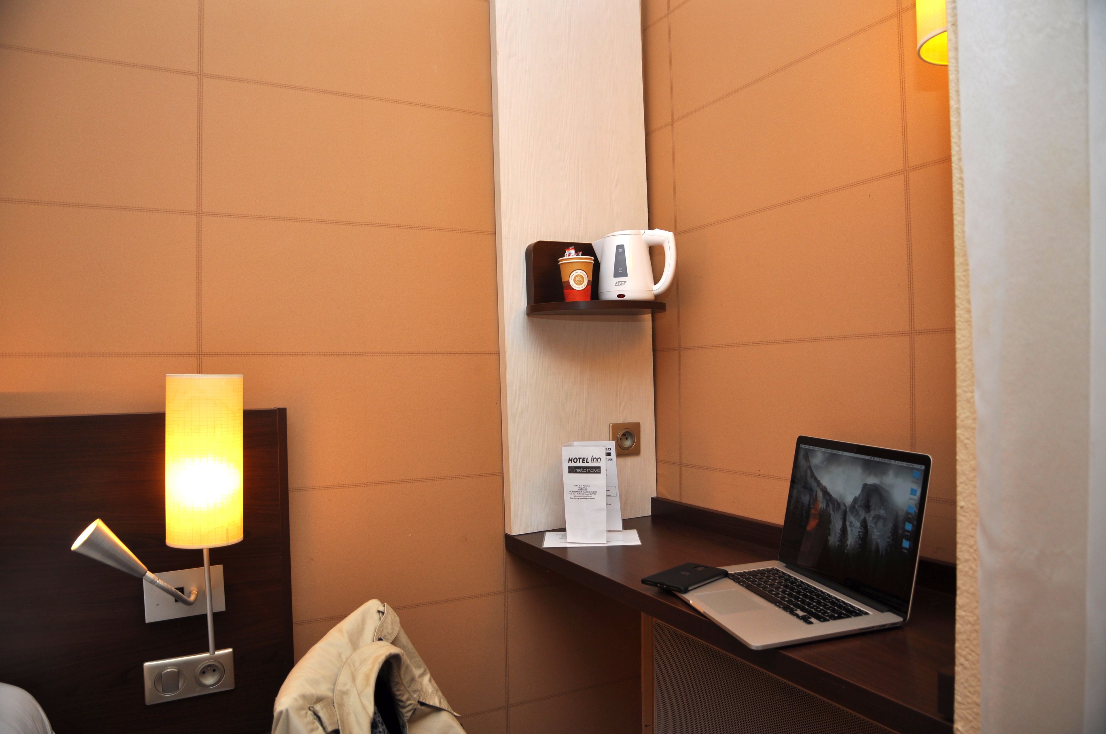 A hotel room with a bed, a desk with a laptop, a coffee machine, and a lamp.