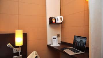 A hotel room with a bed, a desk with a laptop, a coffee machine, and a lamp.