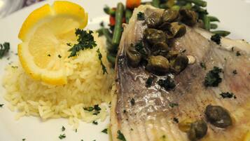 A plate of food with rice, fish, green beans, and capers.