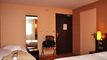 Habitación de hotel con dos camas, una maleta sobre una silla, una puerta y una mesita de noche con una lámpara.