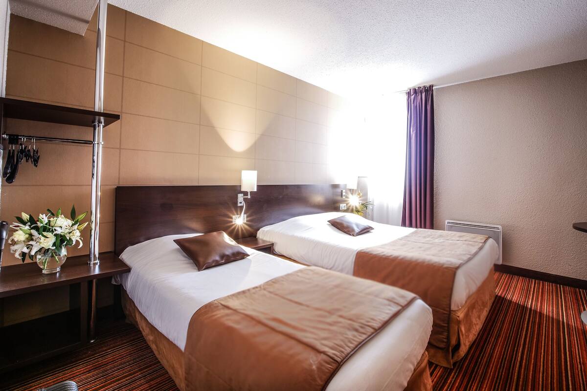 Una habitación de hotel con dos camas, un escritorio con lámpara y un jarrón de flores.