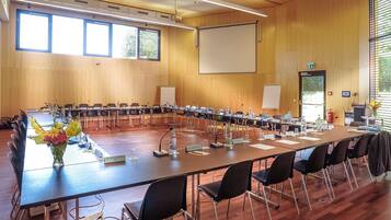 Ein Konferenzraum mit langem Tisch, Namensschildern, Mikrofonen und einer Projektionsleinwand.