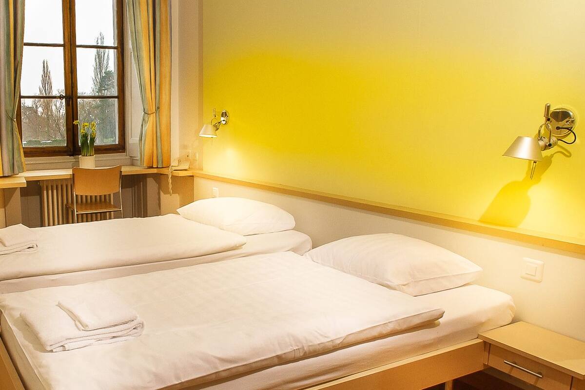 Ein Hotelzimmer mit zwei Betten, einem Schreibtisch und einem Fenster mit Vorhängen.