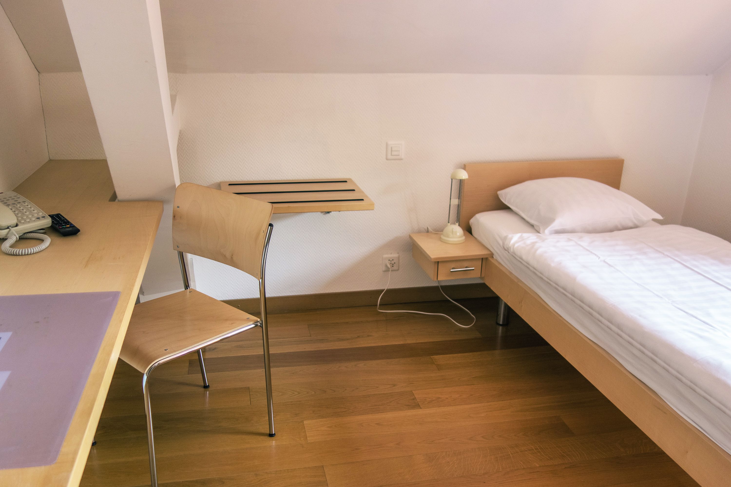 Une chambre à coucher avec un bureau en bois, une chaise, une table de chevet avec une lampe et un lit avec une literie blanche.
