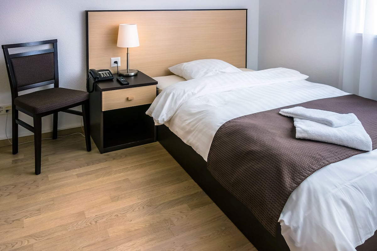 Ein Hotelzimmer mit einem Bett, einem Sessel, einem Nachttisch mit Lampe und einem Telefon.