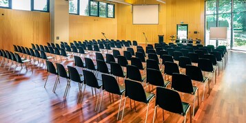 Un salón de conferencias con filas de sillas, un atril y una pantalla grande.