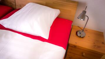 A bed with white and red bedding, a wooden headboard, and a bedside table with a lamp.