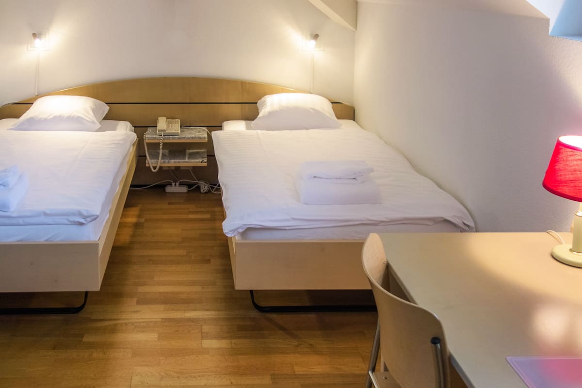 Ein Hotelzimmer mit zwei Einzelbetten, Holzboden, einem Schreibtisch mit Lampe und einem Telefon auf dem Nachttisch.