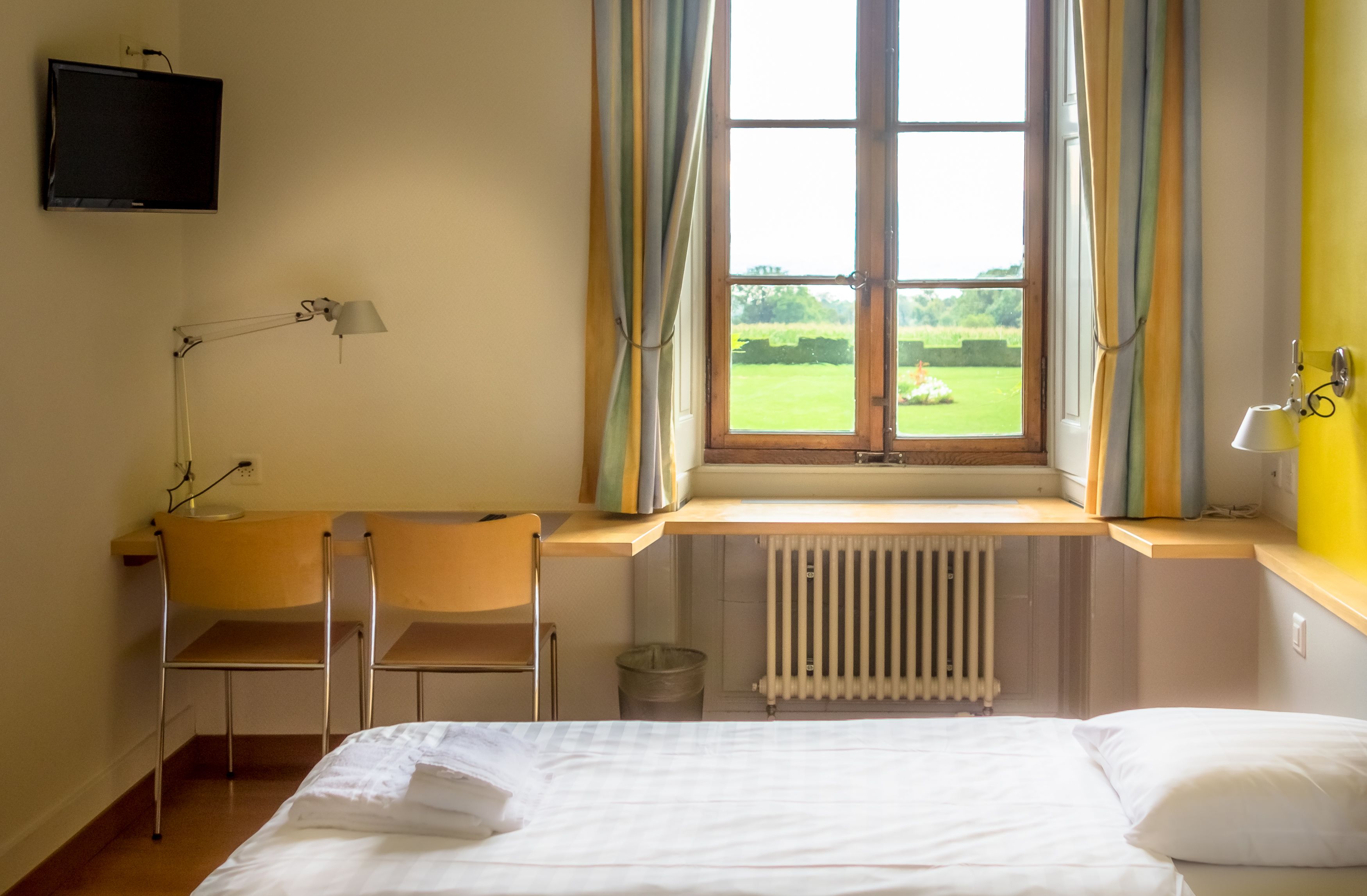 Een hotelkamer met een bed, een bureau met stoel, een aan de muur bevestigde televisie en een raam met gordijnen.