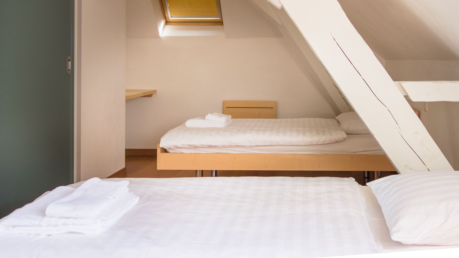 Une petite chambre avec un lit simple, un plafond en pente et un puits de lumière.