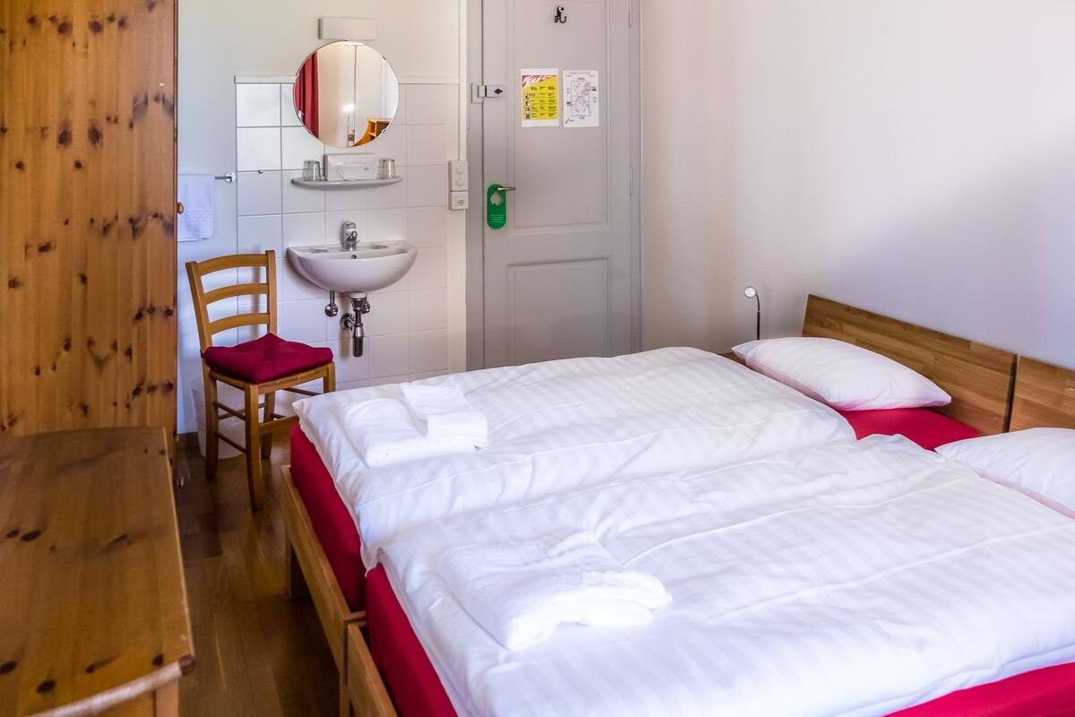 Ein Hotelzimmer mit einem hölzernen Bett, einem Holzstuhl, einem Waschbecken und einem Spiegel.