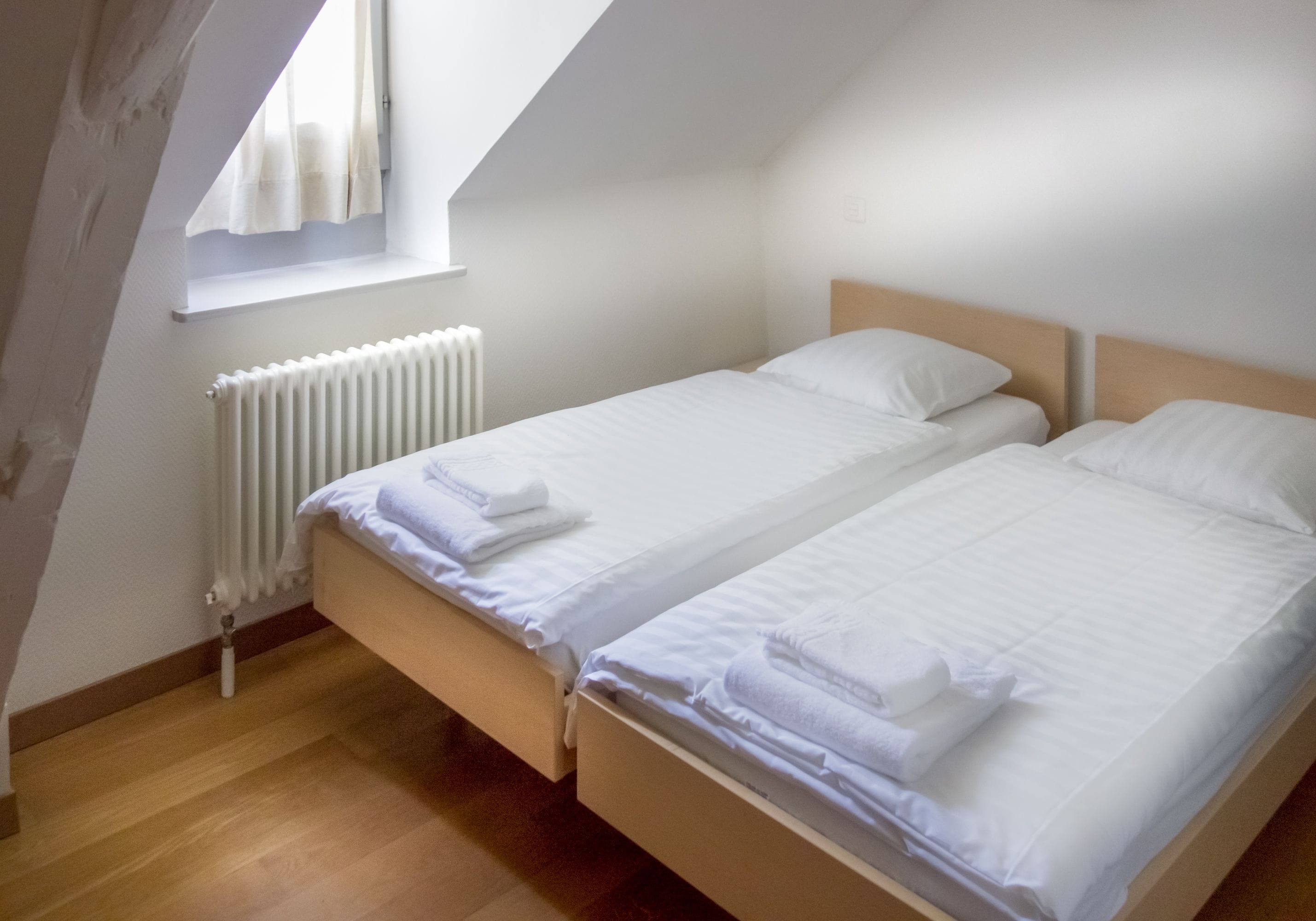 A bedroom with two beds, a radiator, and a window with curtains.