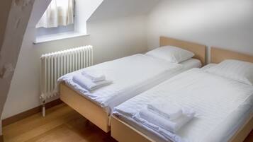 A bedroom with two beds, a radiator, and a window with curtains.