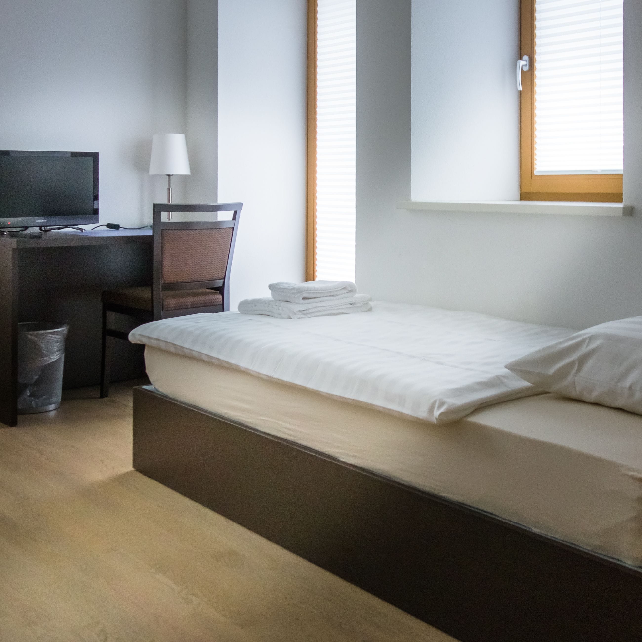 A hotel room with a bed, a desk, a chair, a TV, and a window with blinds.