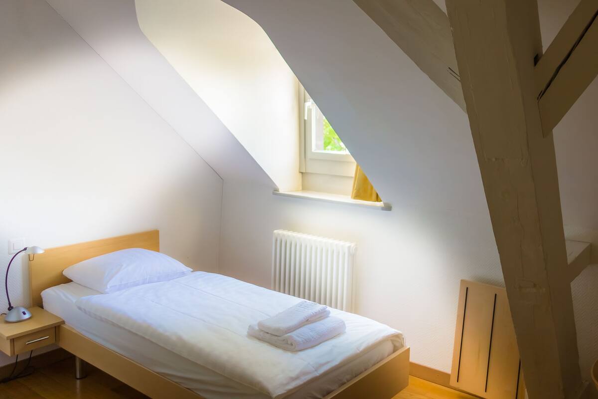 Ein Schlafzimmer mit einem Einzelbett, einem Nachttisch, einer Lampe, einem Fenster und einer Heizung.