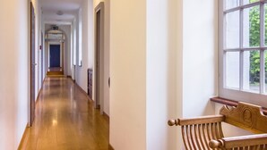 Un long couloir étroit, avec un plancher en bois et des murs blancs. Un banc se trouve sur le côté droit, près d’une fenêtre.
