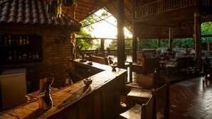 A rustic bar area with wooden furniture, a brick wall, and a thatched roof. - Selous Kinga Lodge (Mloka)