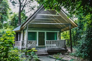 A rustic cabin with a wooden porch, surrounded by dense forest. - Selous Kinga Lodge (Mloka)