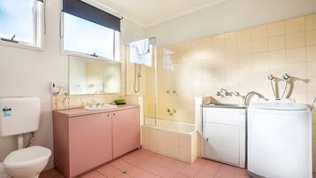 A bathroom with a toilet, sink, vanity, shower, and a washing machine.